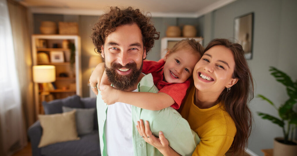 Family of three laughing and hugging, enjoying time together in a domestic setting